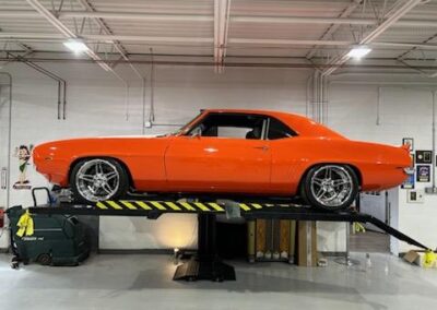reddish orange sports car on a lift inside a building