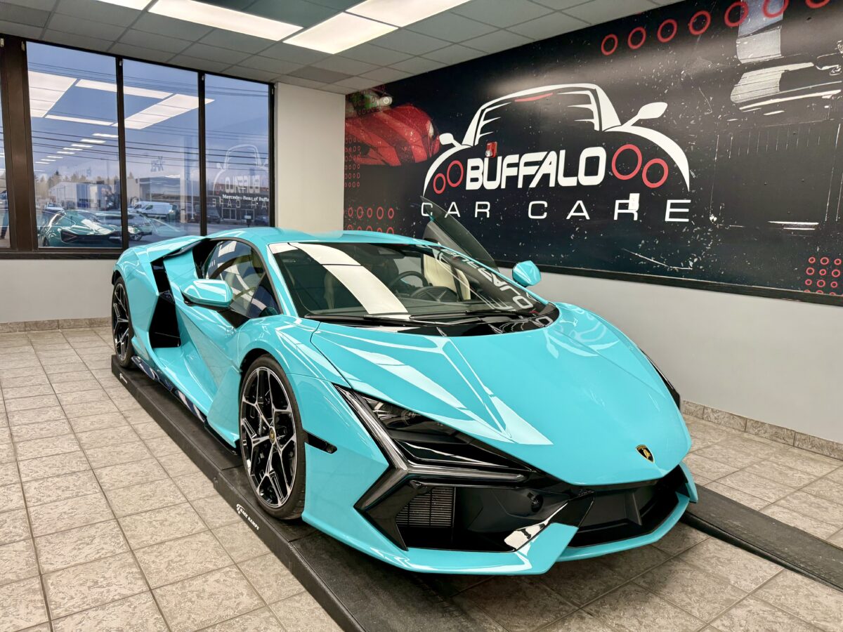 vO47HPmOIkmzNmTABMljnHi28CdHK3RTxw Turquoise luxury sports car in a showroom with large windows and a "Buffalo Car Care" wall sign. Sleek design, modern, and high-performance feel.